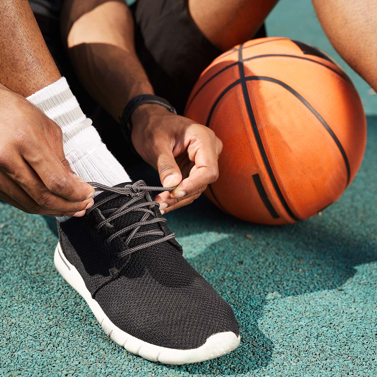 Closeup of African-American man tying sports shoes in basketball court outdoors, copy space background