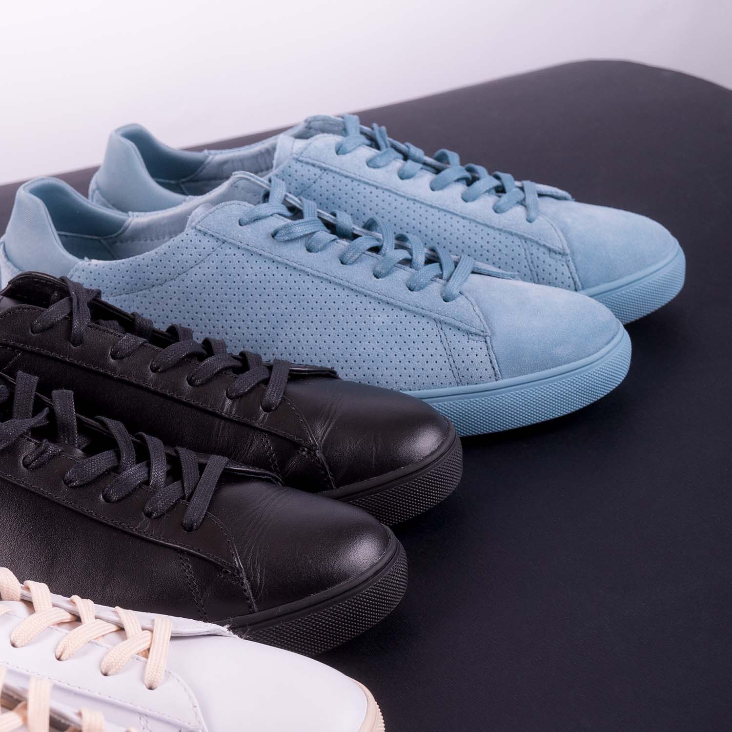 Three pair of sneakers on black background. Black, white and blue shoe