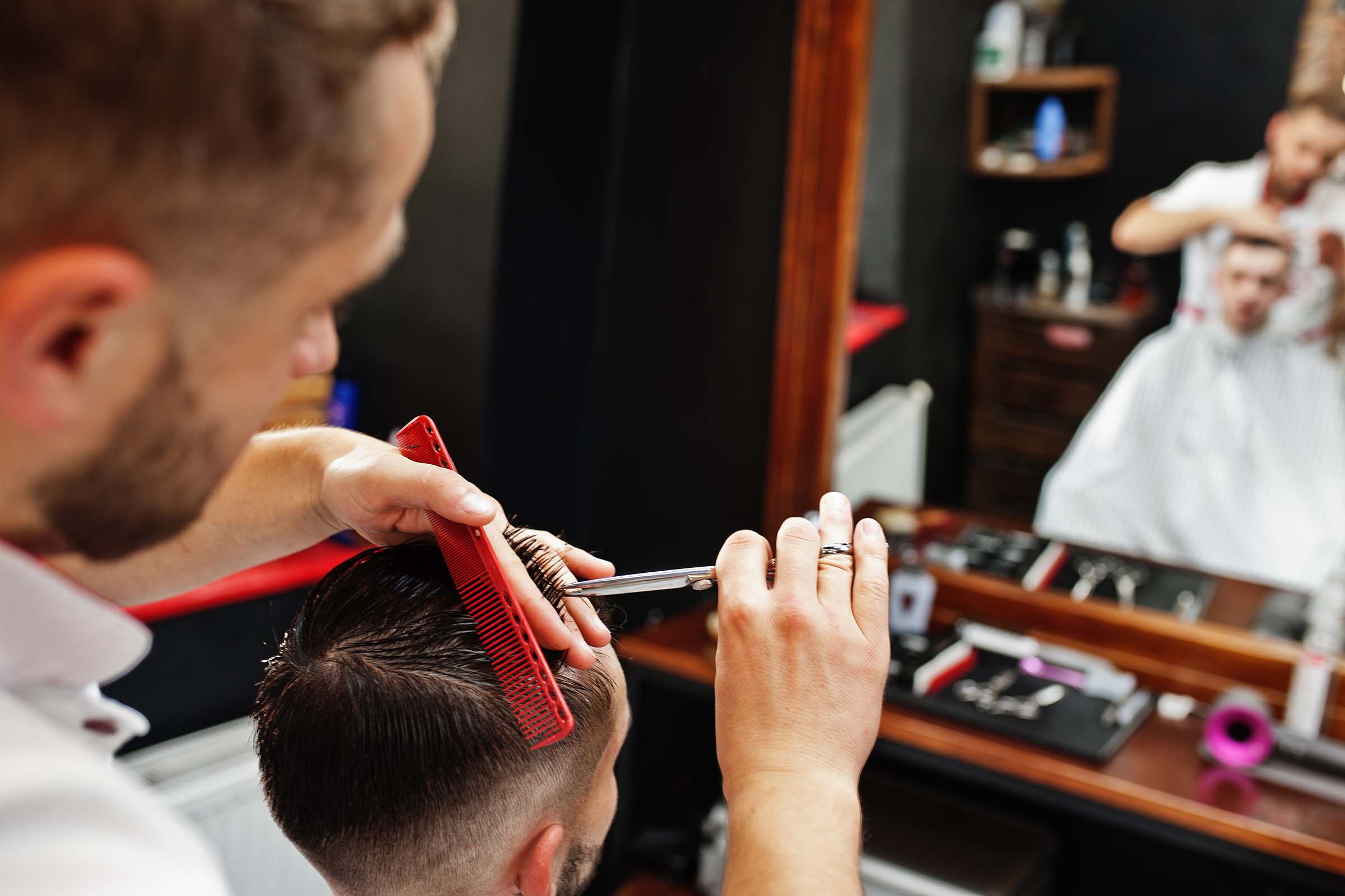 Young bearded man getting haircut by hairdresser while sitting in chair at barbershop. Barber soul.