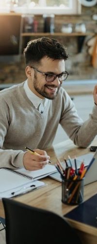 Feliz empresário usando laptop e tomando notas enquanto trabalhava em casa _ Foto Premium