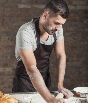 Free Photo _ Male baker rolling dough with rolling pins on kitchen counter